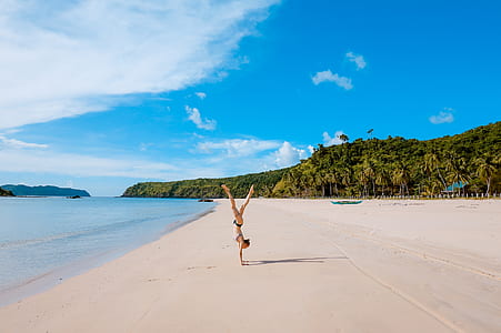 woman cartwheel on brown sand near seashore under blue sky at daytime thumbnail