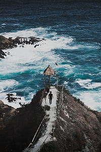 man walking on mountain hill near body of water thumbnail