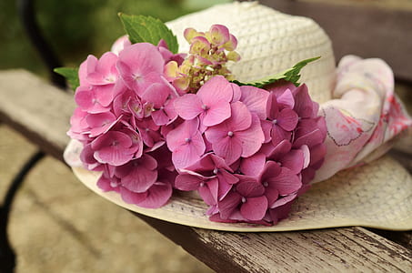 photo of white summer hat with purple petaled flower accent on white wooden surface thumbnail