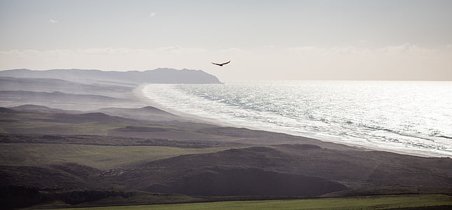 photo of ocean and mountain under cloudy sky thumbnail