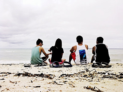 four people sitting on brown sand near beach thumbnail