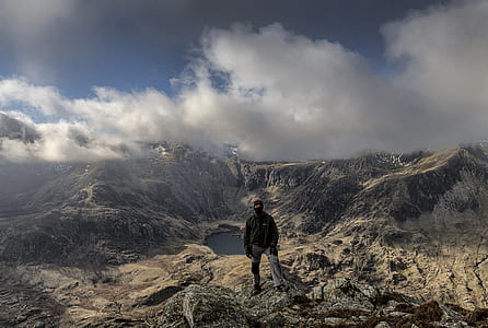 man standing on rocky mountain overlooking lake during daytime thumbnail
