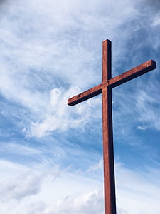 low-angle photo of brown wooden cross under thin white clouds thumbnail