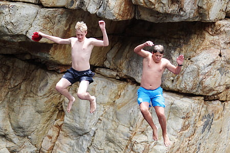 two male jumping on rock cliff during daytime thumbnail