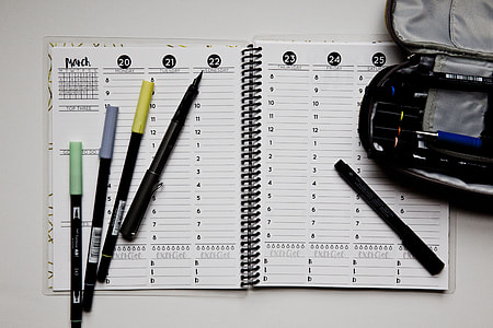 open notebook with five assorted pens on white white surface thumbnail