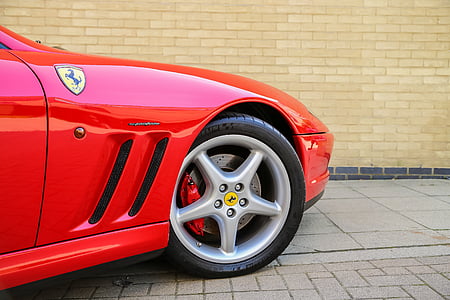 red Ferrari sports car on gray pavement near beige wall thumbnail