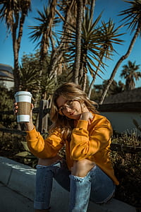 woman sitting beside the road holding cup with lid during day thumbnail