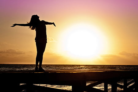 silhouette of woman spreading hand standing on port near body of water with sunset view thumbnail