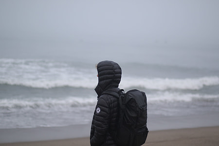 person in hoodie standing on seashore during day thumbnail