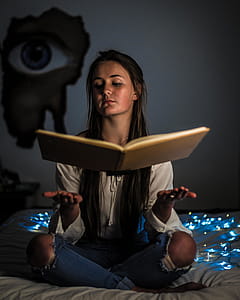 Woman Reading a Book Sitting on Mattress Near the Blue String Light Inside the Room thumbnail