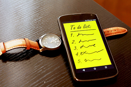 black smartphone on top of round silver analog watch with orange strap thumbnail
