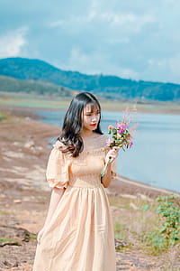 Shallow Focus Photography of Woman in Beige Off-shoulder Dress Holding Bouquet of Flowers thumbnail