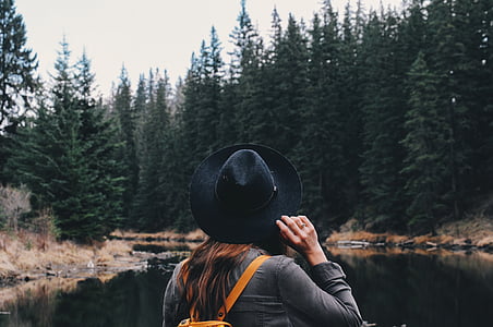 woman holding her hat and facing on trees thumbnail