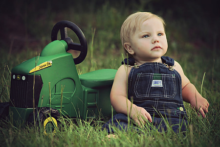 baby sitting on grass field against John Deere ride-on toy thumbnail