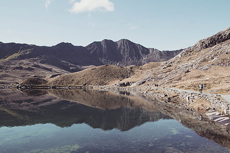 man walking beside body of water near mountains thumbnail