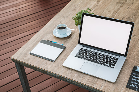 MacBook Pro turned on on top of brown wooden table near the teacup with saucer thumbnail