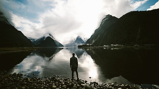 silhouette photo of man in front of water and mountain thumbnail