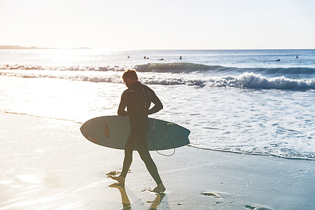 A surfer walks on the beach on his way down to the sea, image captured in Cornwall, England thumbnail