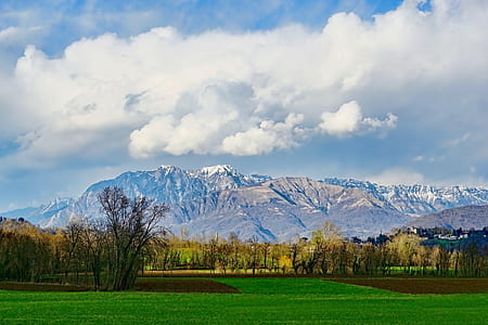 green grass field overlooking snow capped mountain under white cloudy skies at daytime thumbnail