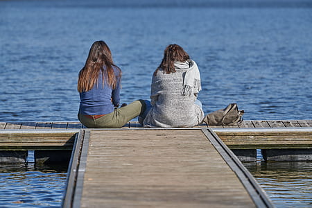 two woman sitting on dock watching sea thumbnail
