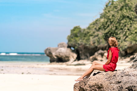 woman in red rompers sitting on rock looking at sea thumbnail