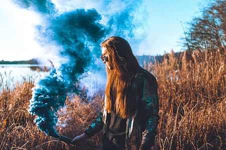 man holding flare near brown grass field and body of water during daytime thumbnail