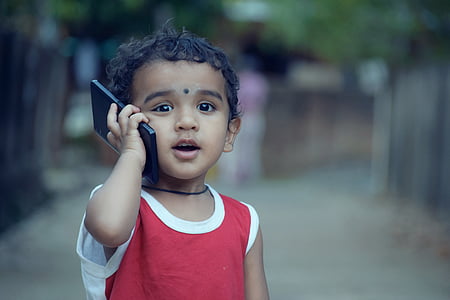 shallow focus photography of toddler in red top holding black smartphone thumbnail