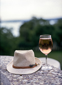 beige fedora hat beside wine glass on brown concrete platform during daytime in tilt shift lens photography thumbnail