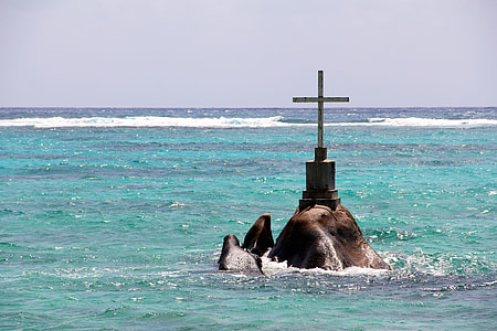 brown cross on rock between body of water at daytime thumbnail