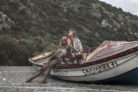 two women sitting on canoe near mountain during daytime thumbnail