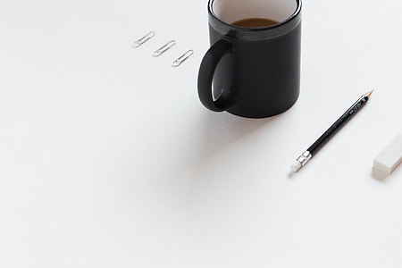 three gray paper clip beside black ceramic coffee mug and pencil on white surface close-up photo thumbnail