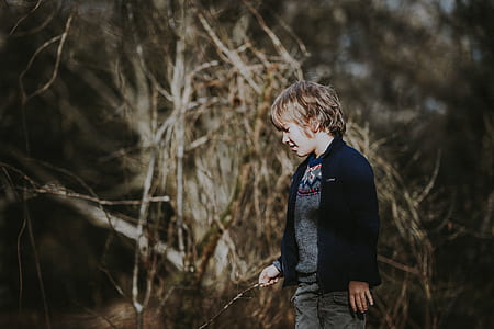 boy holding stick looking down near tree branches thumbnail