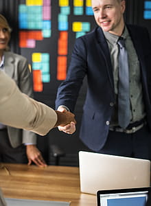 Man Wearing Black Suit Jacket Shaking Hands With Person Wearing Beige Jacket thumbnail