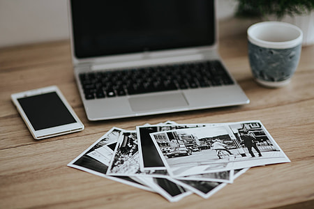 Black-and-white photos with a silver laptop, a smartphone, car keys, pencils and a camera thumbnail