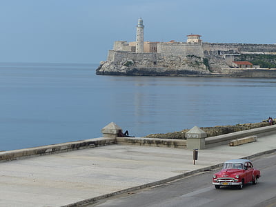 red car passes on road near body of water thumbnail