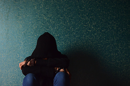 person in black hooded apparel and blue denim jeans sitting hiding his face between hands photo thumbnail