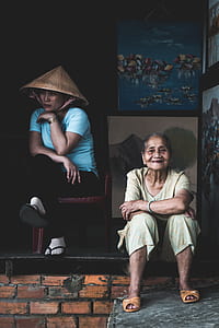 smiling woman sitting on floor beside woman sitting on monobloc chair thumbnail