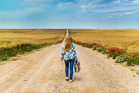 woman wearing a blue jeans and floral long-sleeve shirt while walking in the middle on the road during daytime thumbnail