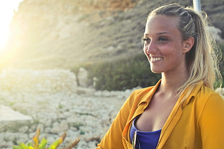 A young blonde woman in yellow button-up shirt and blue tank top posing in the sun with smile thumbnail
