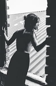 topless woman with black skirt standing on window grayscale photography thumbnail