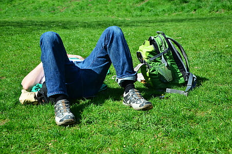 person lying on green grass beside green backpack thumbnail