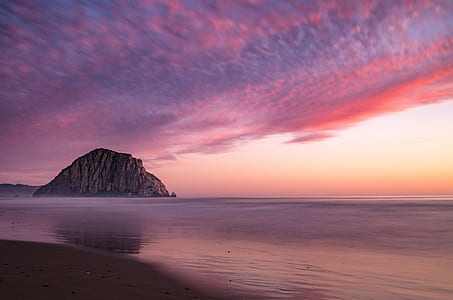 brown rock formation beside body of water under cloudy sky thumbnail