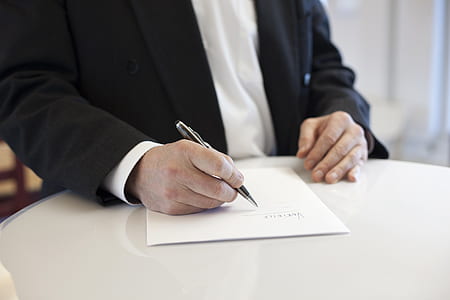 man holding gray twist pen writing on white printer paper thumbnail