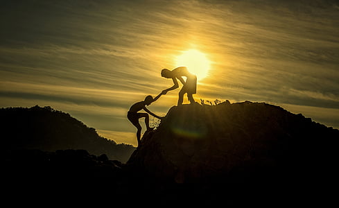silhouette of man helping another man to climb on cliff during golden hour thumbnail
