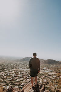 man standing on cliff facing village during daytime thumbnail