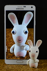 white Samsung Android smartphone and white figurine on brown surface thumbnail