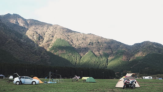 white car on green field near camping tents and mountain during daytime thumbnail