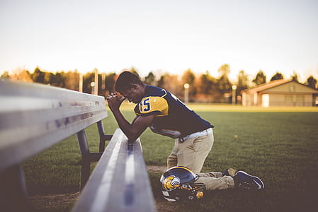 man in yellow and black football jersey shirt kneeling while praying during daytime thumbnail