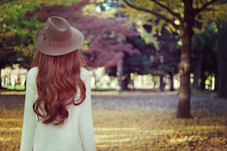 woman wearing hat and white long sleeved dress standing near tall trees at daytime thumbnail