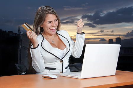 woman in white blazer holding card while looking at MacBook white thumbnail
